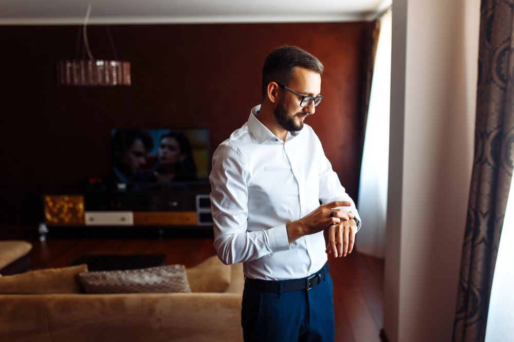 Muškarac u svetloj košulji i elegantnim pantalonama sprema se za letnju svadbu u modernom enterijeru.